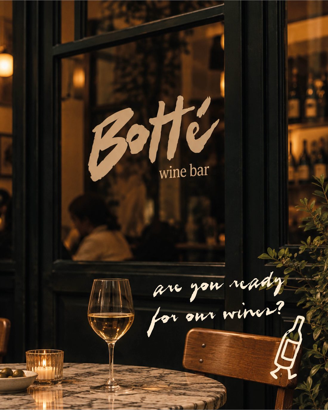 The window of Botté wine bar at night, with a glass of white wine on a marble table